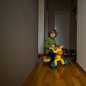 Child riding a colorful toy tricycle in a cozy indoor hallway.